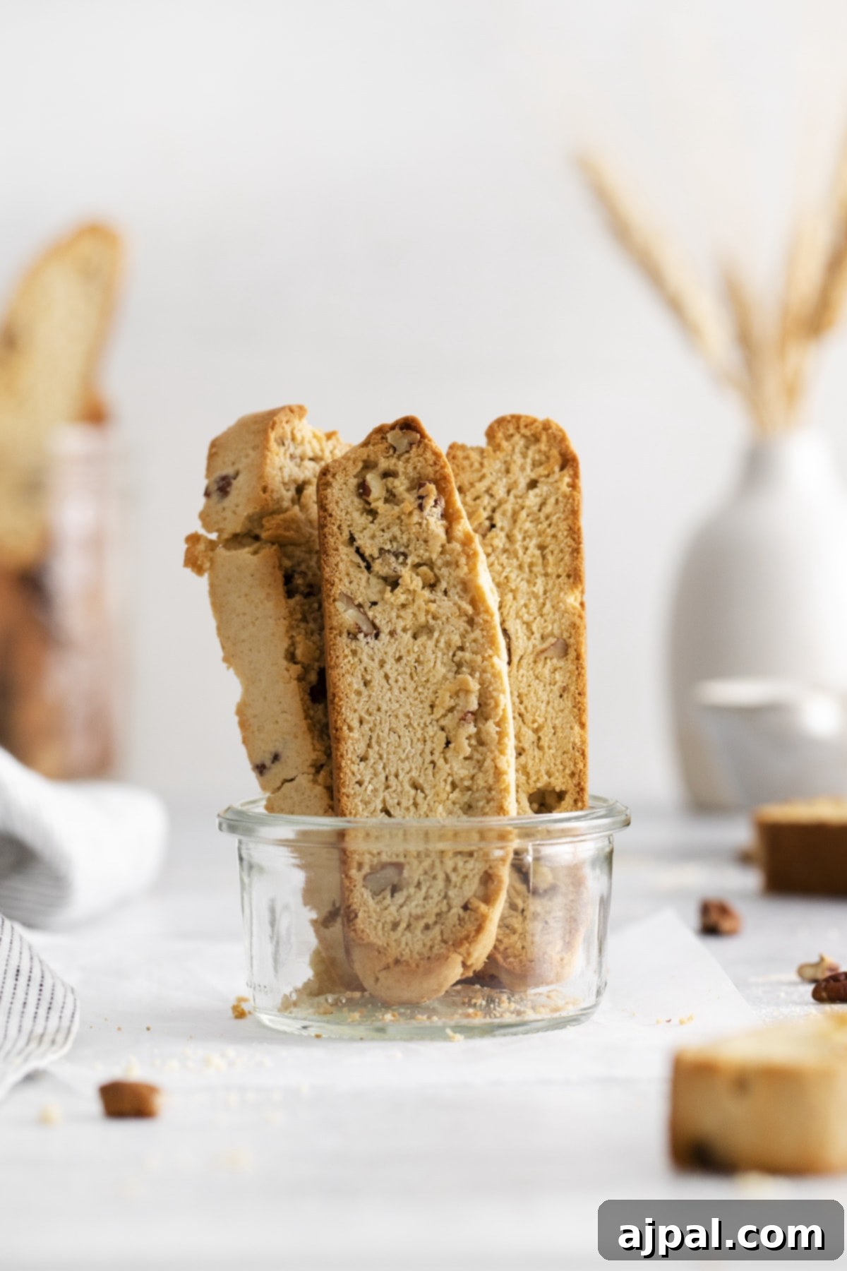Golden Maple Pecan Biscotti 3 Baked maple pecan biscotti, golden brown and studded with pecans, arranged in a clear glass bowl on a white table.