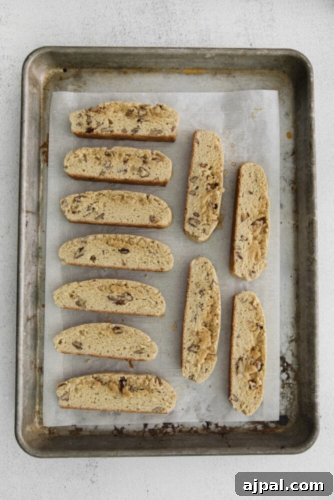 Golden Maple Pecan Biscotti 9 Sliced maple pecan biscotti pieces laid cut-side down on a baking sheet, ready for their second bake.