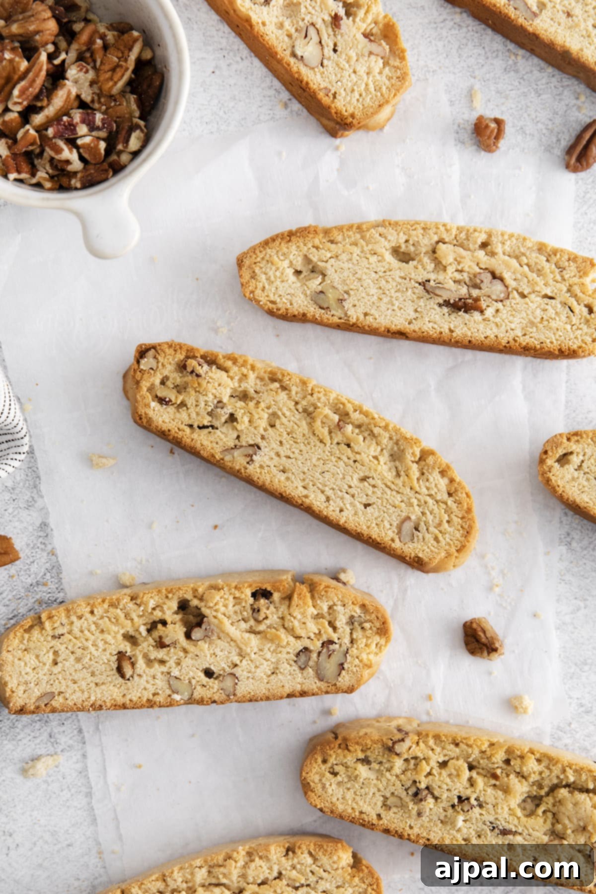 Golden Maple Pecan Biscotti 10 Close-up of golden brown maple pecan biscotti pieces arranged on a sheet of parchment paper, with scattered pecans around them.