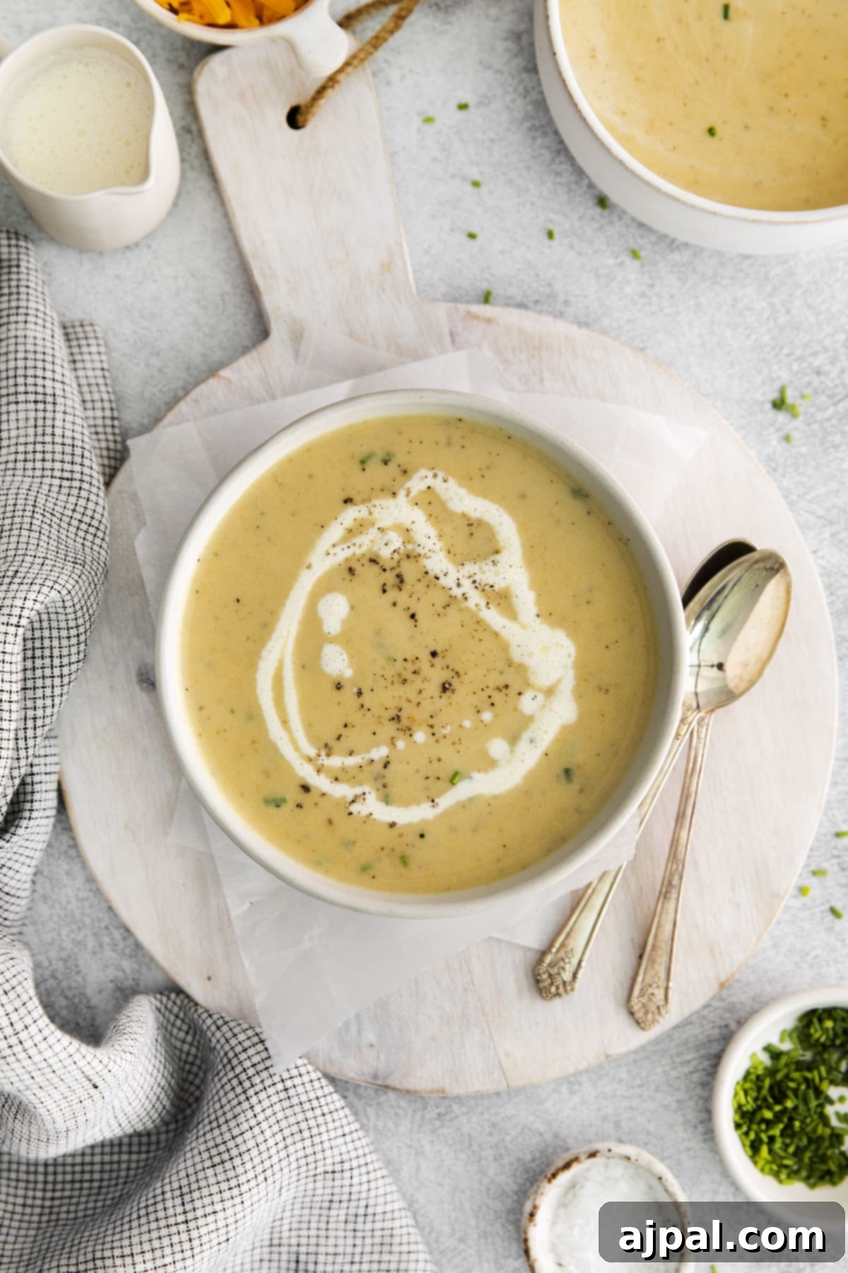 A spoon resting next to a rustic bowl of creamy apple cheddar soup, garnished with a delicate swirl of fresh cream and a sprinkle of cracked black pepper, inviting warmth and comfort.