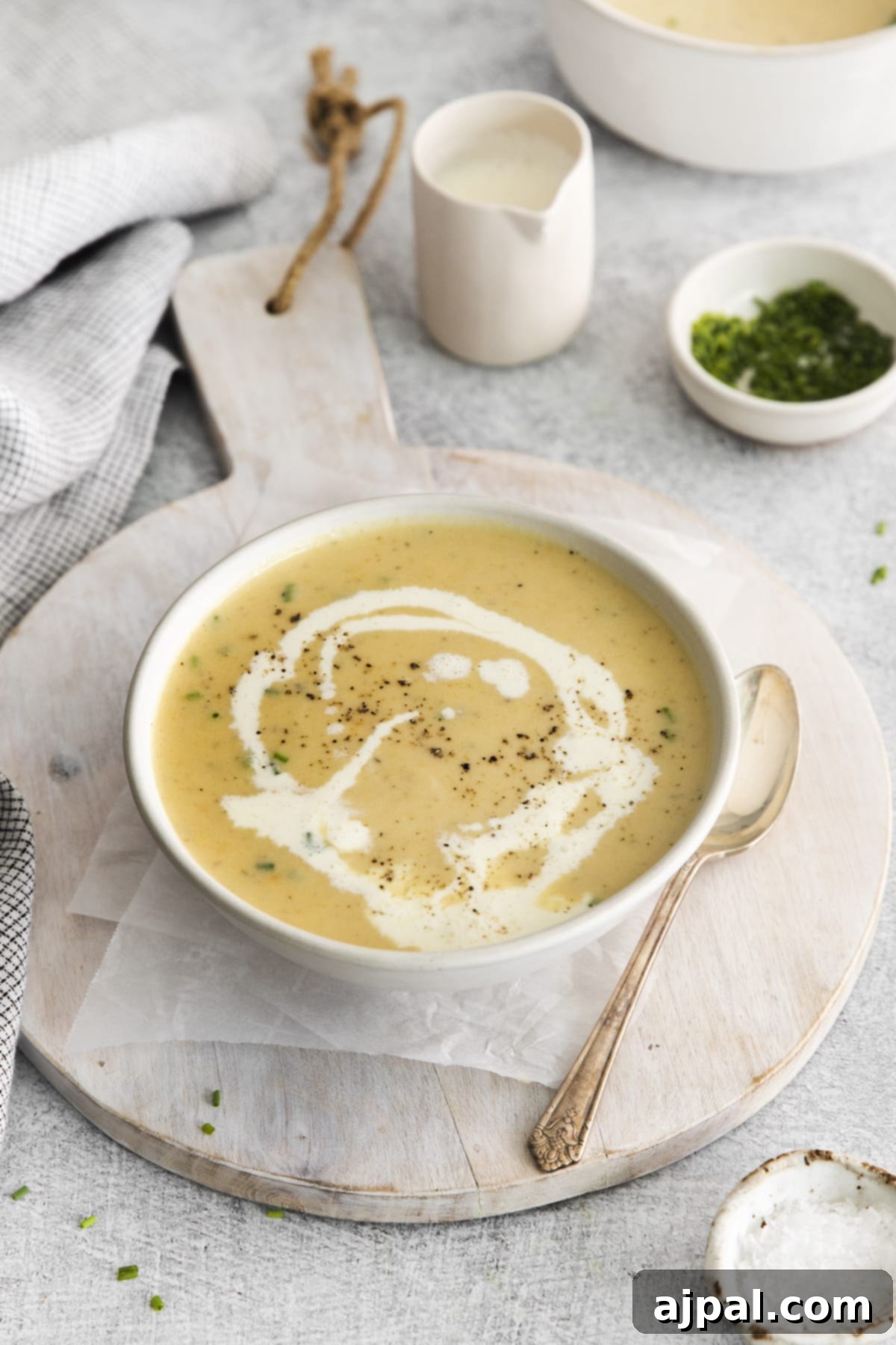A delightful bowl of apple cheddar soup, exquisitely garnished with a swirl of cream and a touch of cracked pepper, presented artfully on a wooden cutting board.