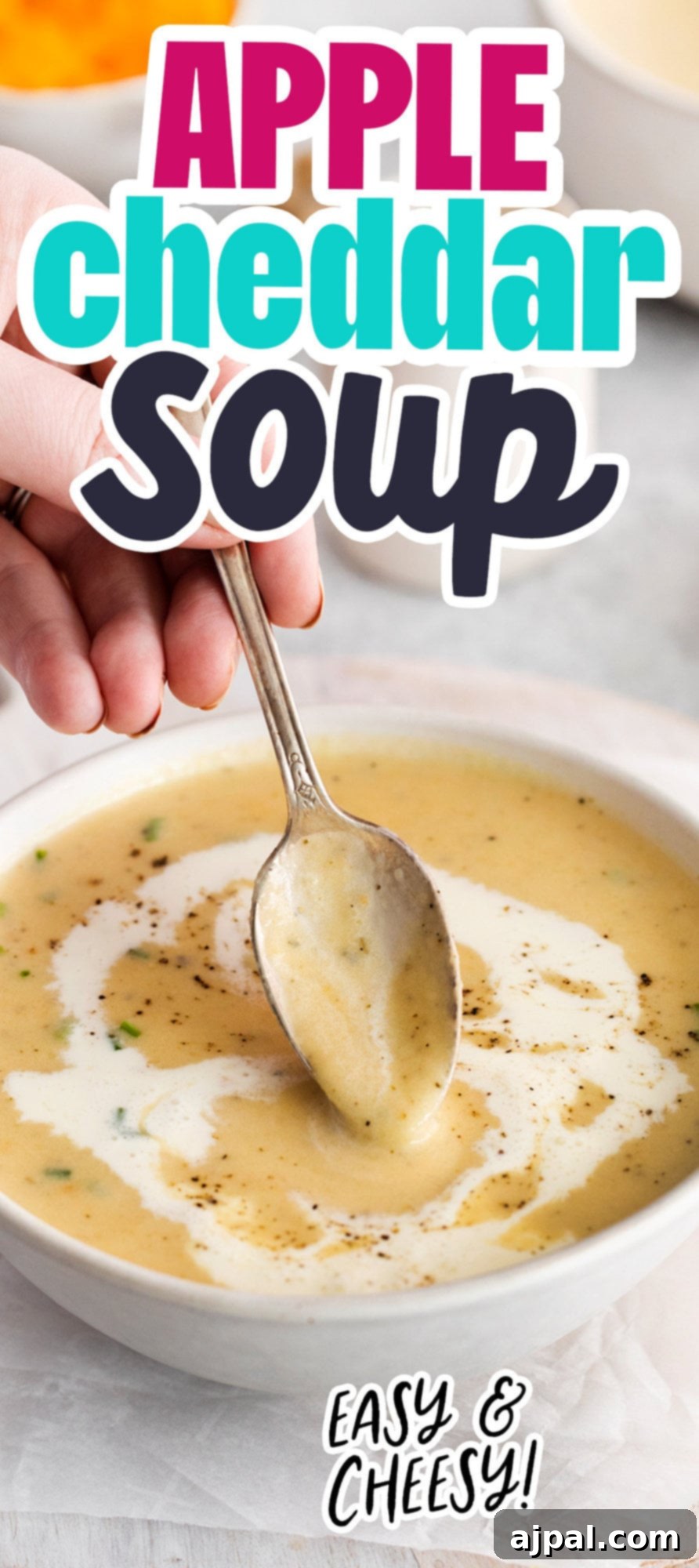 A hand gently dips a spoon into a comforting bowl of creamy apple cheddar soup, highlighting the rich texture, garnished with a swirl of cream and a touch of cracked pepper on top.