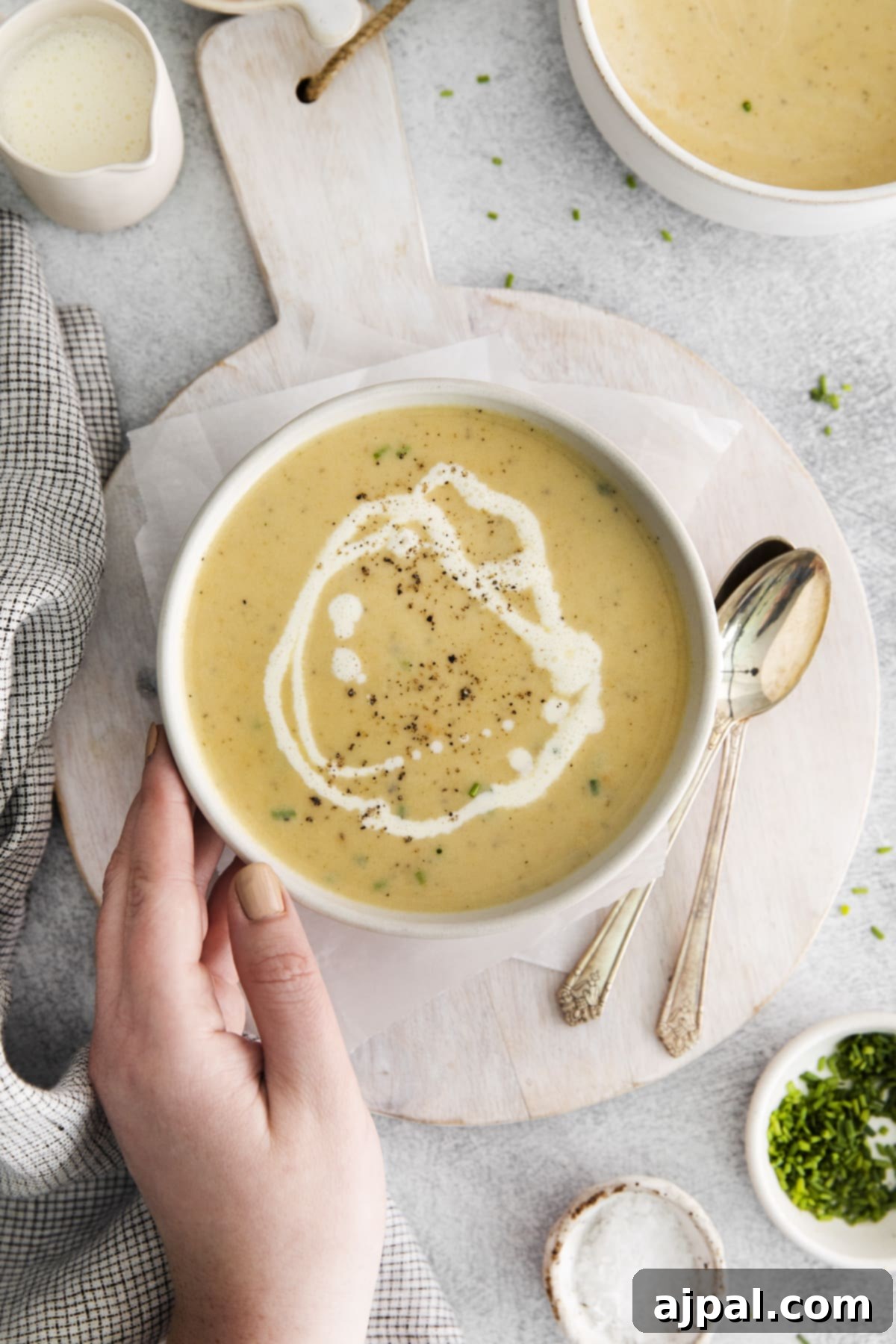 A bowl of creamy apple cheddar soup, perfectly garnished with a swirl of cream and a crack of pepper, presented on a wooden surface.