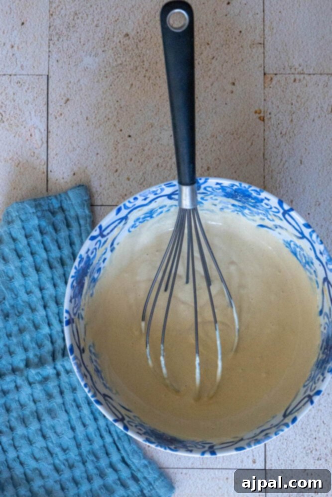 A whisk actively blending tahini sauce in a bowl, creating a smooth and creamy consistency.