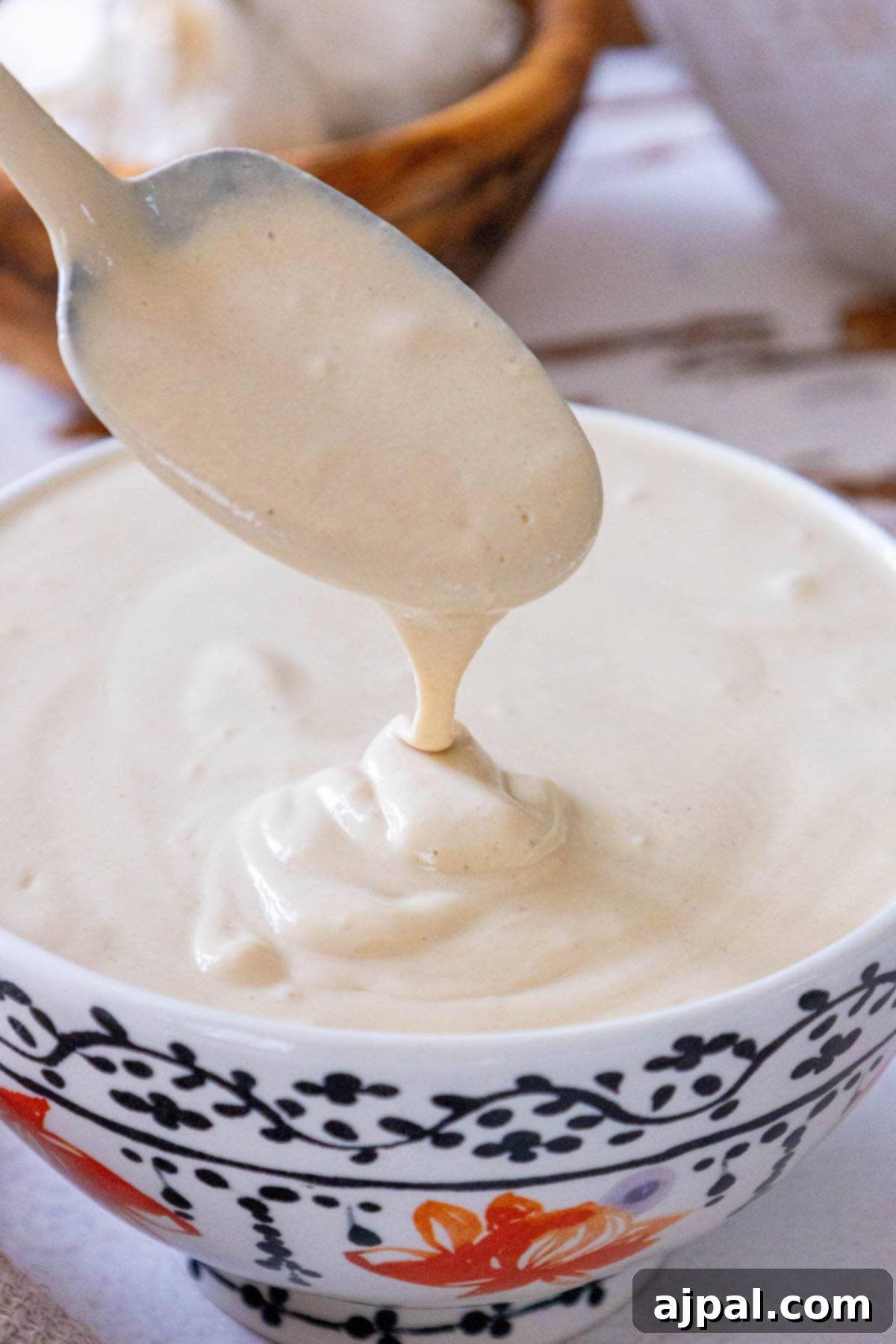 A spoon pouring luscious tahini sauce into a serving bowl on a textured table.