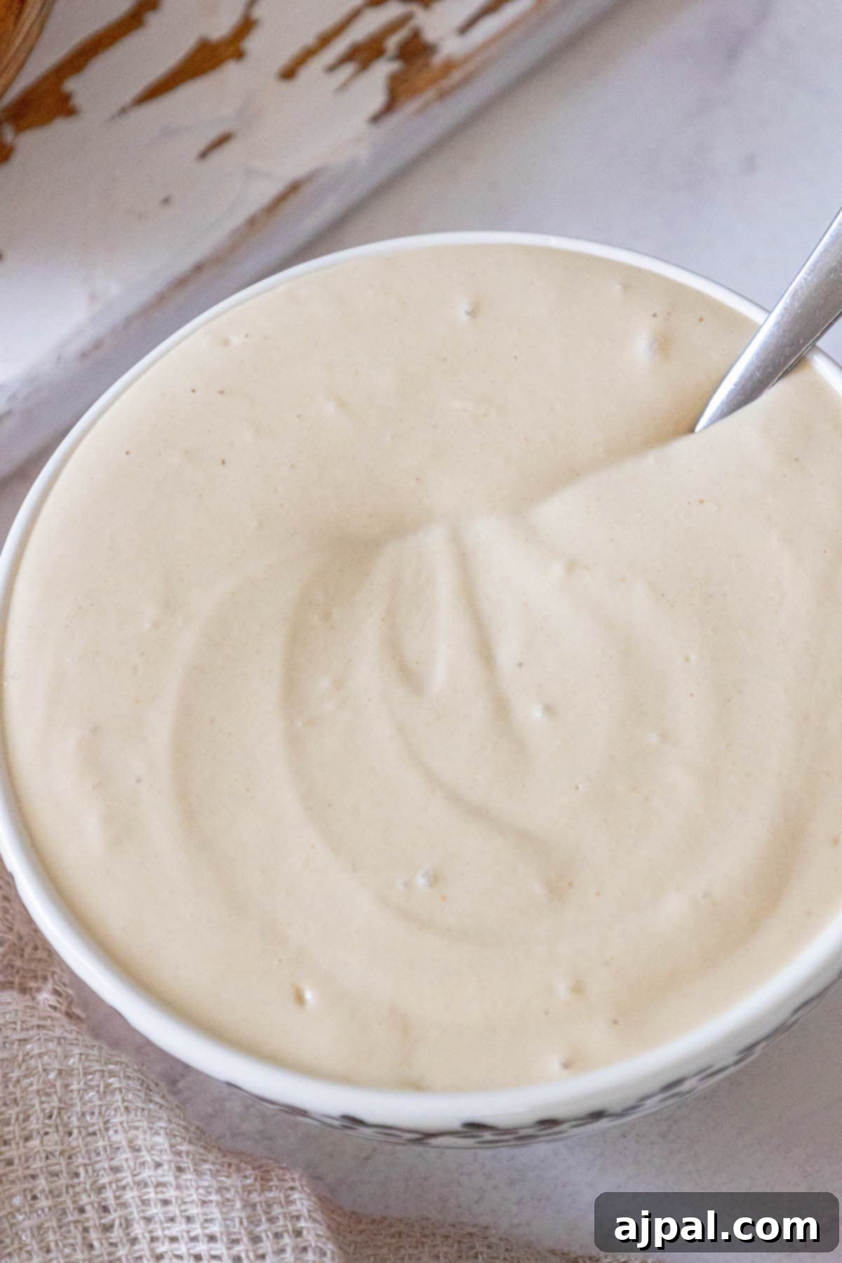 A pristine white bowl holding creamy garlic tahini sauce, with a spoon resting inside, ready for dipping.