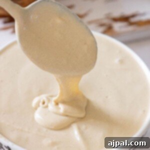 A spoon delicately lifting creamy tahini sauce over a bowl, illustrating its perfect, smooth consistency on a rustic wooden surface.