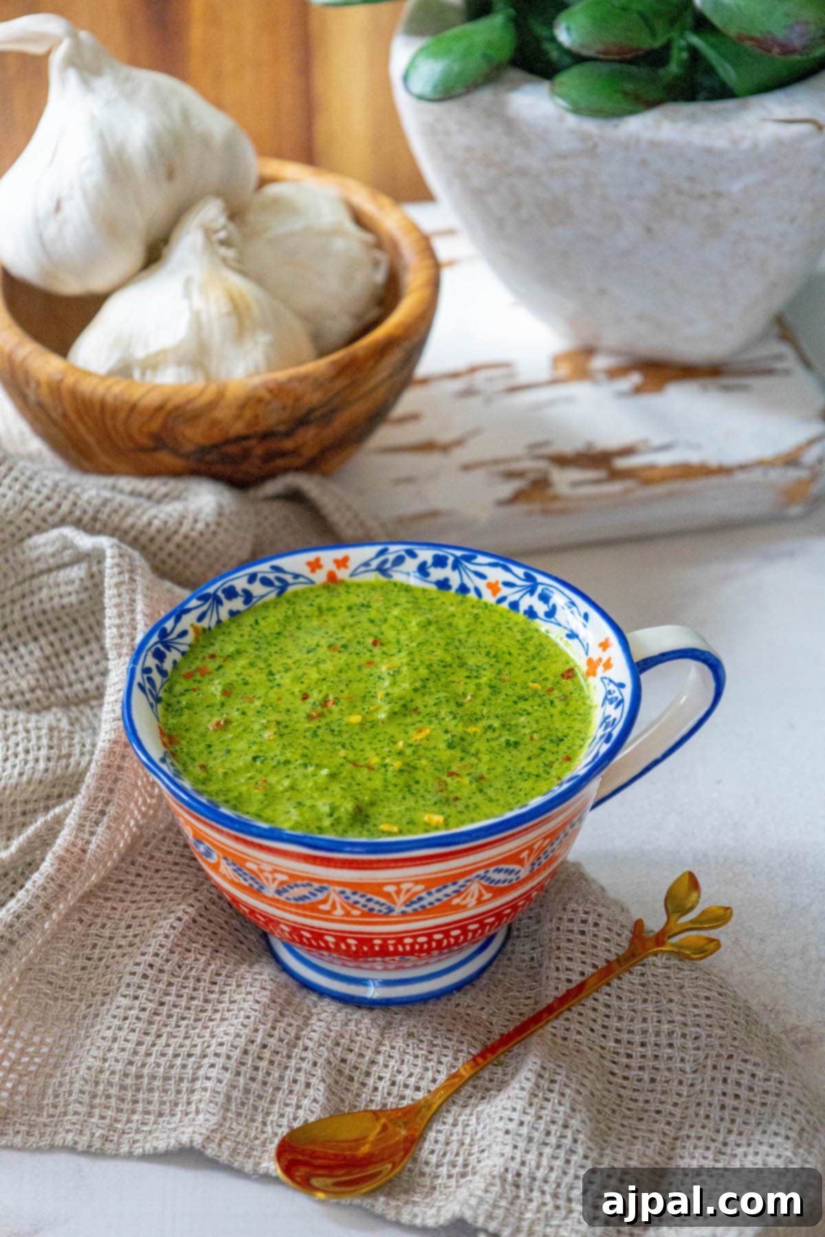 Skhug Zhoug Sauce Recipe 15 Bright green zhoug sauce, speckled with flecks of fresh cilantro and vibrant red pepper flakes, is presented in a charming mug on a rustic table, inviting a flavorful addition to any meal.