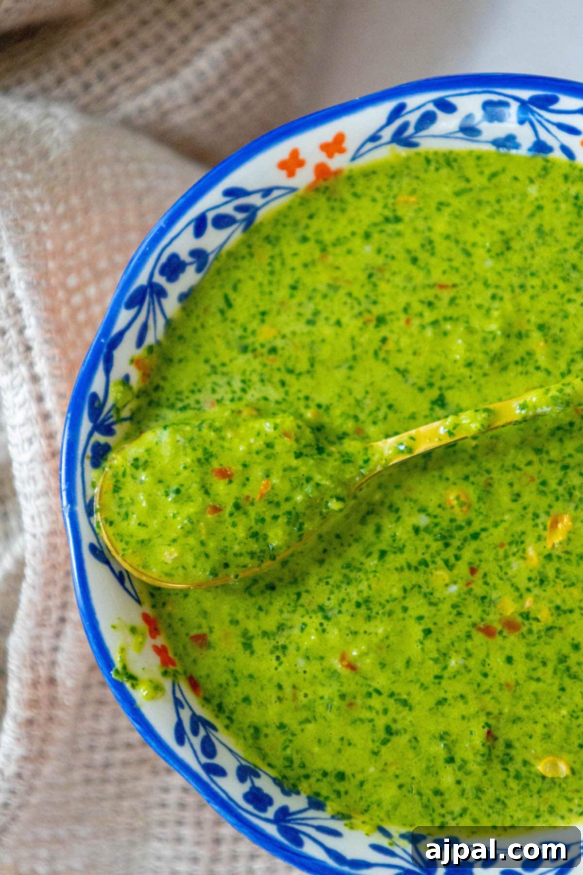 Skhug Zhoug Sauce Recipe 18 Bright green zhoug sauce, accented with flecks of fresh cilantro and vibrant red pepper flakes, is presented in a charming decorative blue mug, perfectly crafted and ready to be enjoyed with any meal.