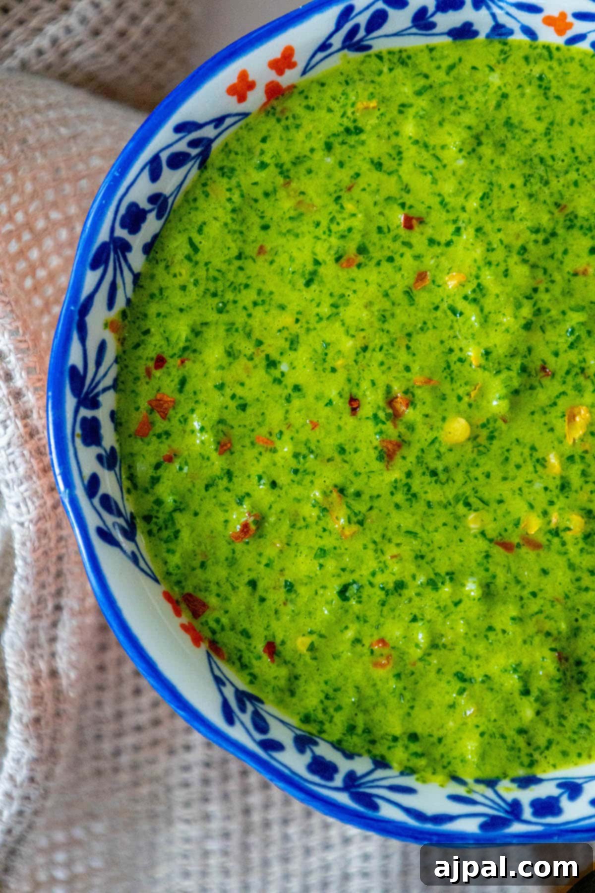 Skhug Zhoug Sauce Recipe 19 Bright green zhoug sauce, with visible flecks of fresh cilantro and vibrant red pepper flakes, elegantly presented in a decorative blue mug, ready to be drizzled over your next culinary creation.