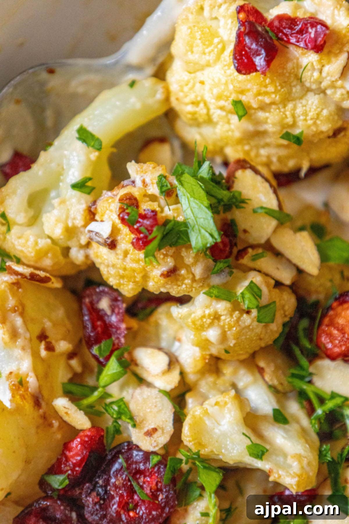 Roasted cauliflower tossed in tahini sauce with cranberries, almonds, and chopped parsley in a white dish, showcasing a healthy and flavorful meal.