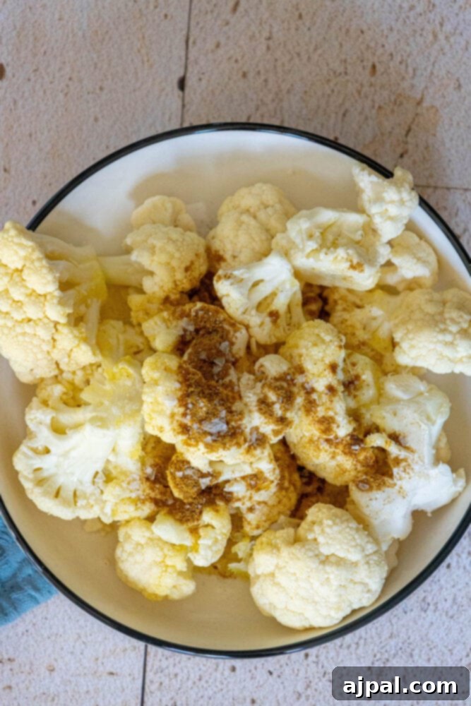 Cauliflower florets prepared in a bowl with olive oil, aromatic herbs, and a sprinkle of salt, ready for roasting.
