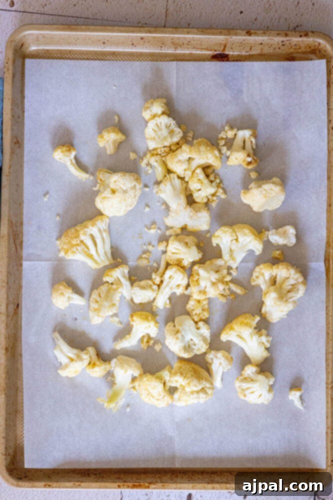 Seasoned cauliflower florets neatly arranged on a baking sheet lined with parchment paper, prepped for roasting.