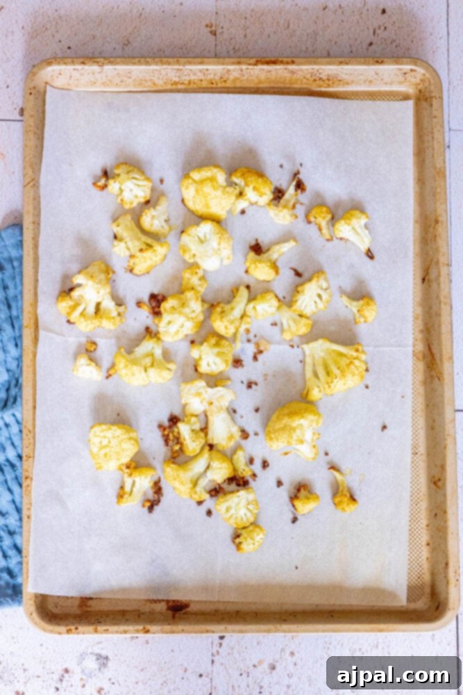 Golden-brown, roasted and seasoned cauliflower florets arranged on a baking sheet lined with parchment paper, just out of the oven.