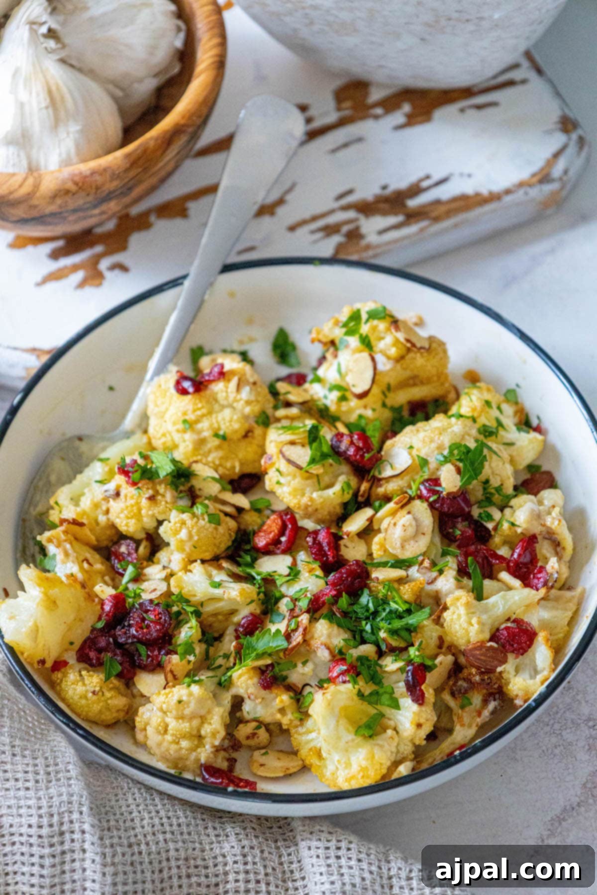 Roasted cauliflower salad tossed in tahini sauce with cranberries, almonds, and chopped parsley in a white dish, ready to be served as a healthy and flavorful side.