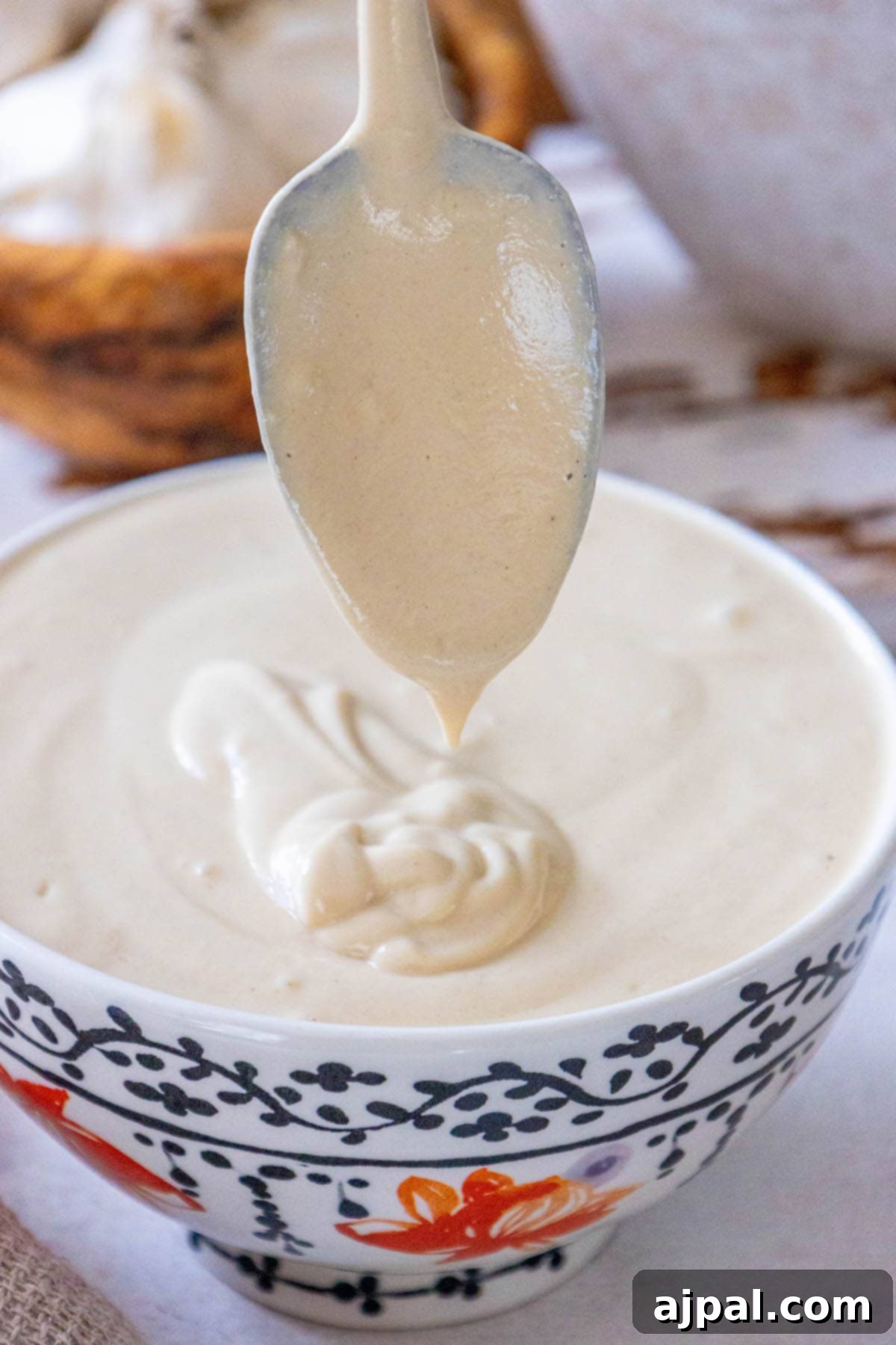 A spoon is being dipped into a bowl of garlic tahini sauce.