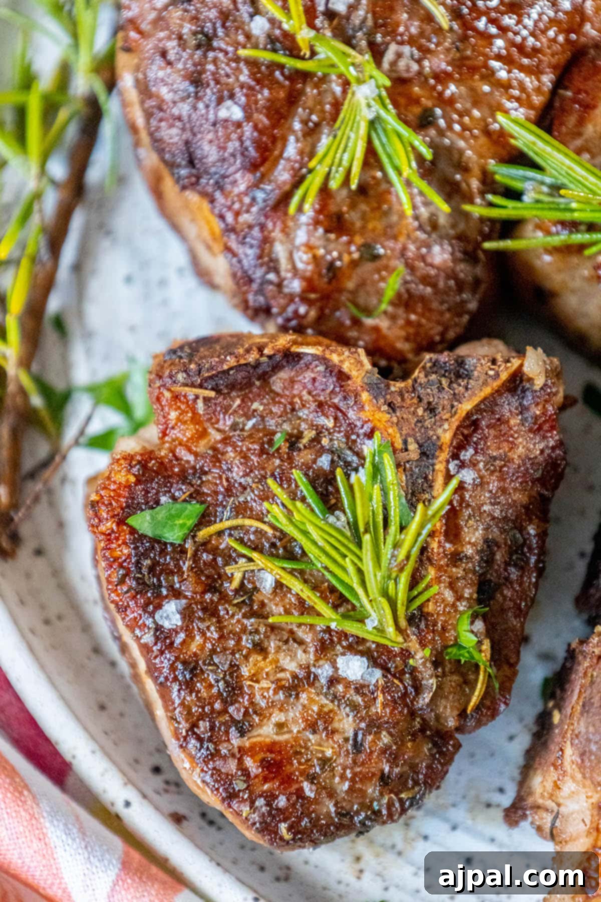 seared lamb chop on a white plate with a sprig of rosemary and sea salt flakes on top 