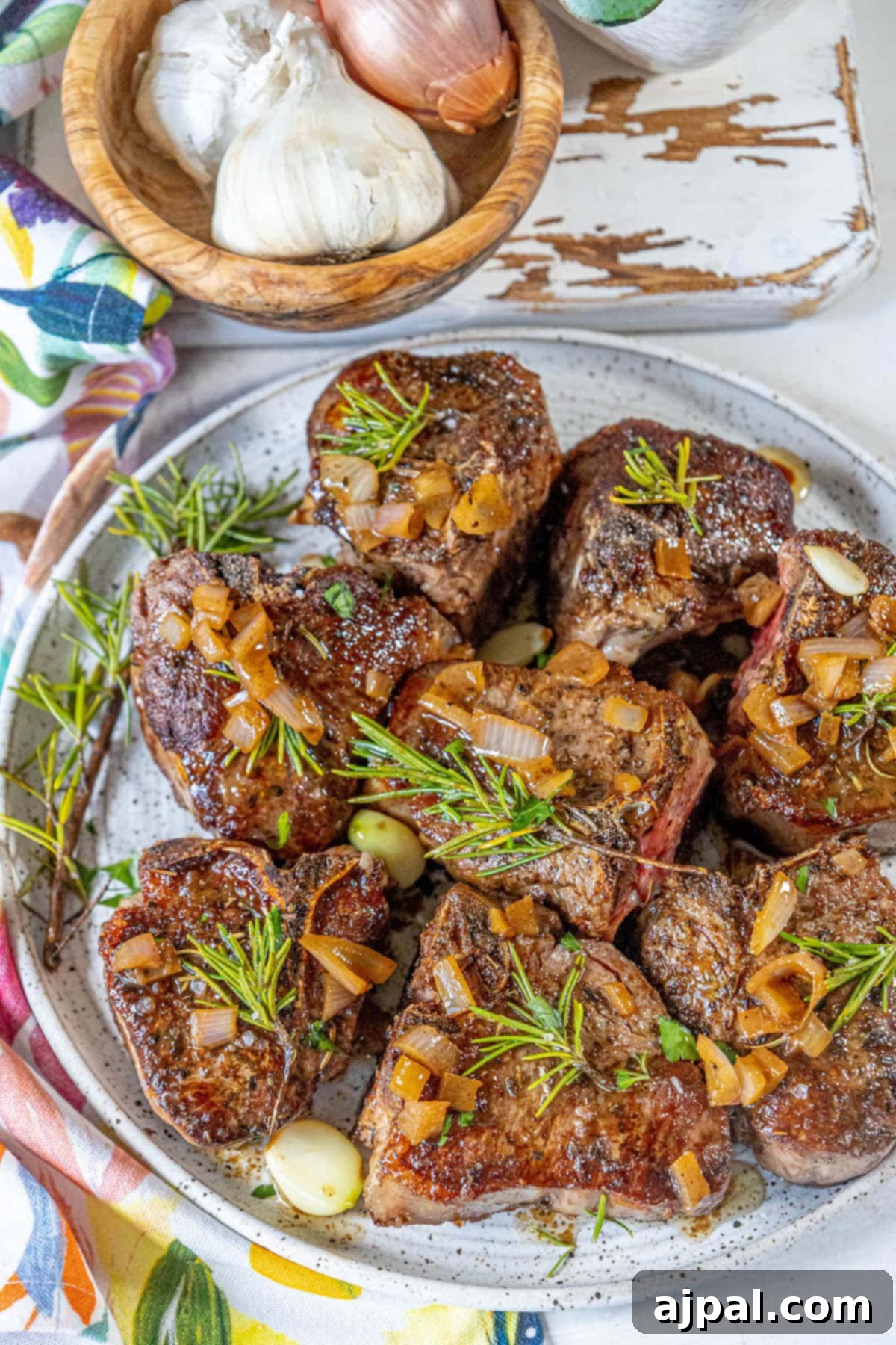 seared lamb chop on a white plate with a sprig of rosemary and sea salt flakes and a white wine shallot sauce on top