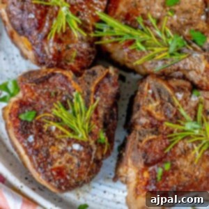 seared lamb chop on a white plate with a sprig of rosemary and sea salt flakes and a white wine shallot sauce on top