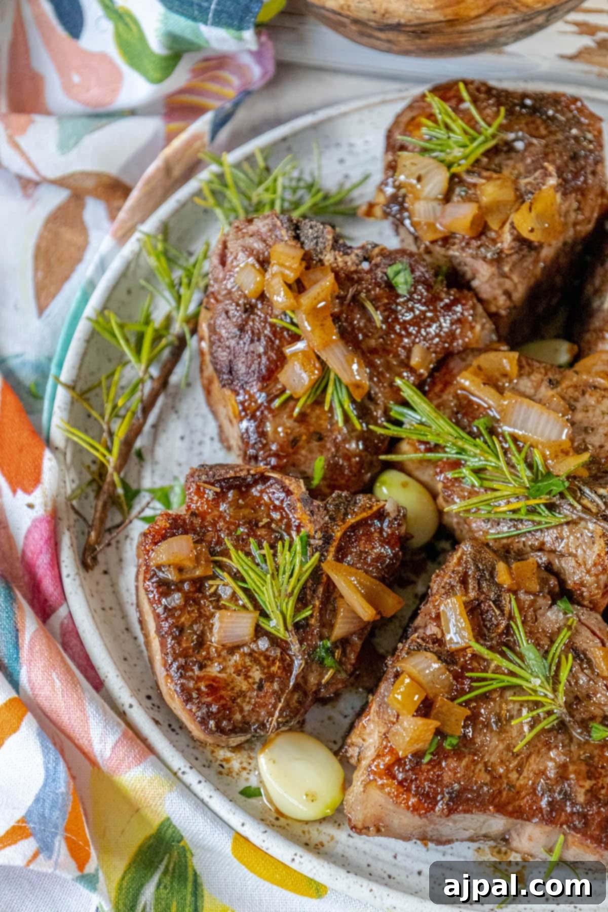 seared lamb chop on a white plate with a sprig of rosemary, garlic cloves, a white wine sauce, and sea salt flakes on top 