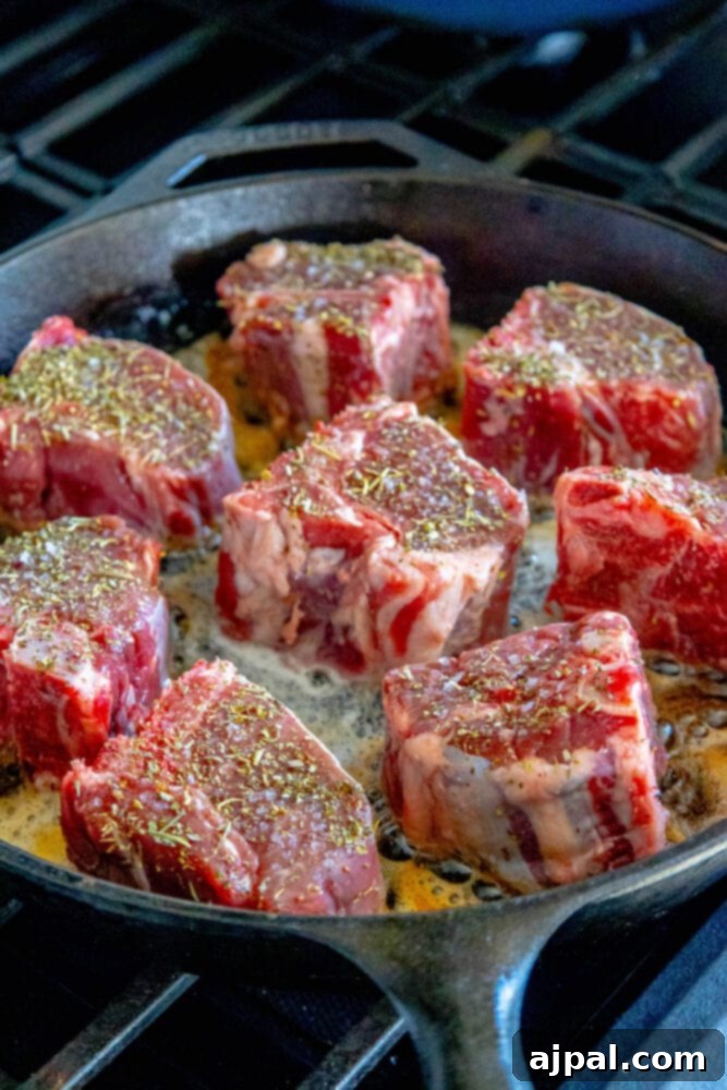 seasoned raw lamb chops in a cast iron pan with melted butter