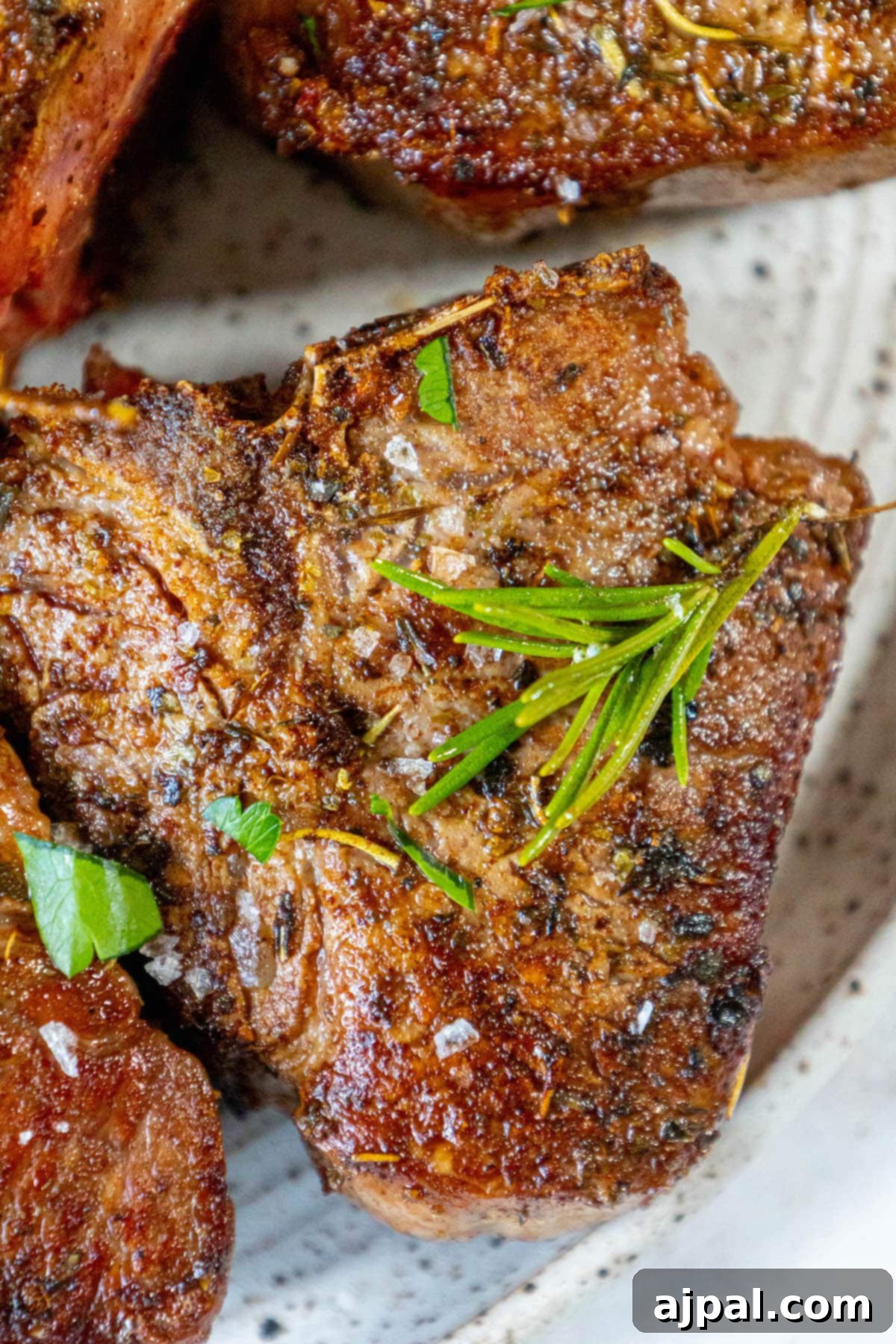 seared lamb chop on a white plate with a sprig of rosemary and sea salt flakes on top 