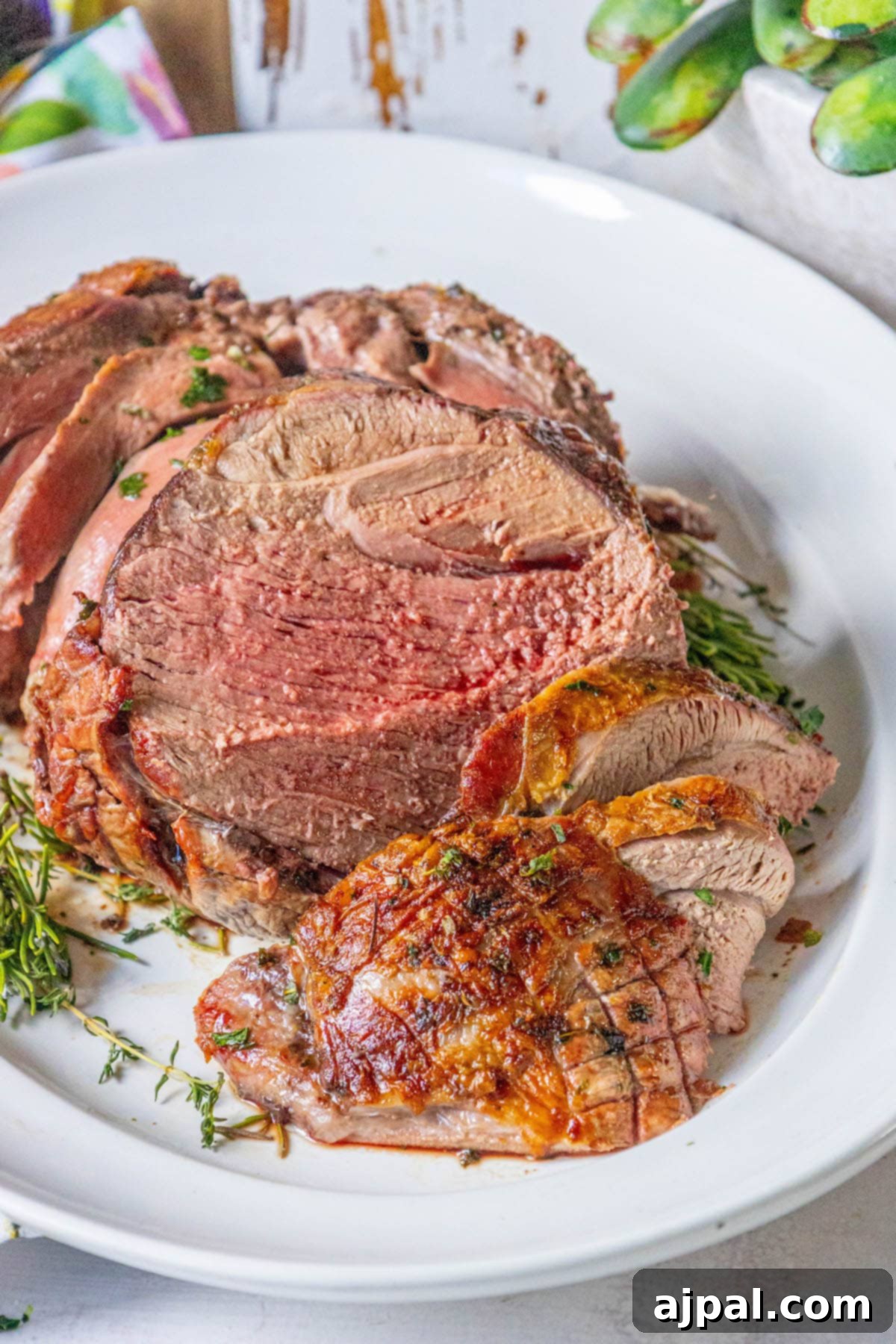 The Ultimate Easy Roasted Leg of Lamb 3 A roasted leg of lamb adorned with fresh rosemary and thyme, presented on a pristine white plate, showcasing its golden-brown crust and juicy interior.