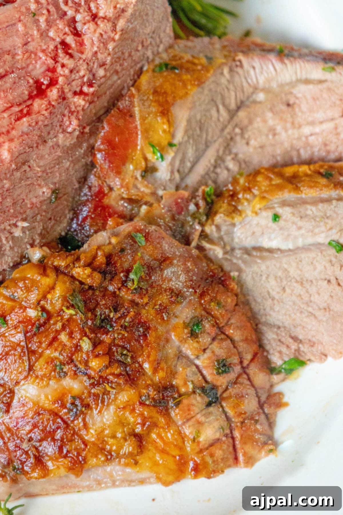 The Ultimate Easy Roasted Leg of Lamb 4 A succulent roasted leg of lamb, expertly sliced and arranged on a white platter, garnished with vibrant chopped herbs, signifying a perfectly cooked meal.