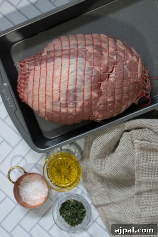 The Ultimate Easy Roasted Leg of Lamb 5 Raw boneless leg of lamb, carefully trussed in netting, sits beside a bowl of rich olive oil, a sprinkle of sea salt, and a vibrant blend of fresh herbs, all arranged on a rustic wooden table.