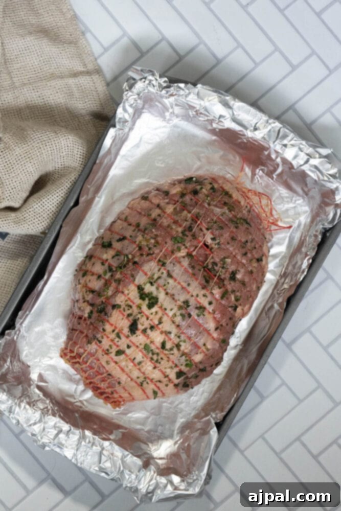 The Ultimate Easy Roasted Leg of Lamb 6 The raw leg of lamb, glistening with a generous coating of olive oil, aromatic herbs, and coarse sea salt, showcasing how to properly season the meat for optimal flavor.