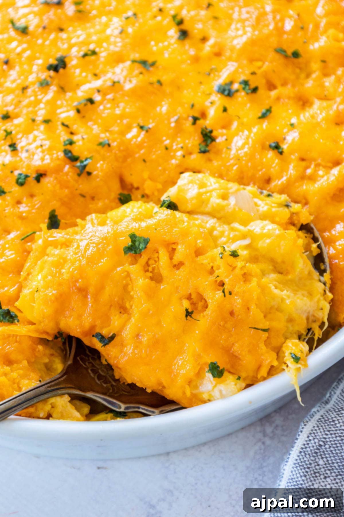 Savory Roasted Squash Gratin 3 A hearty serving of cheesy squash casserole, freshly baked in a white ceramic dish, gleaming with melted cheese and crisp cracker topping, garnished with green herbs.