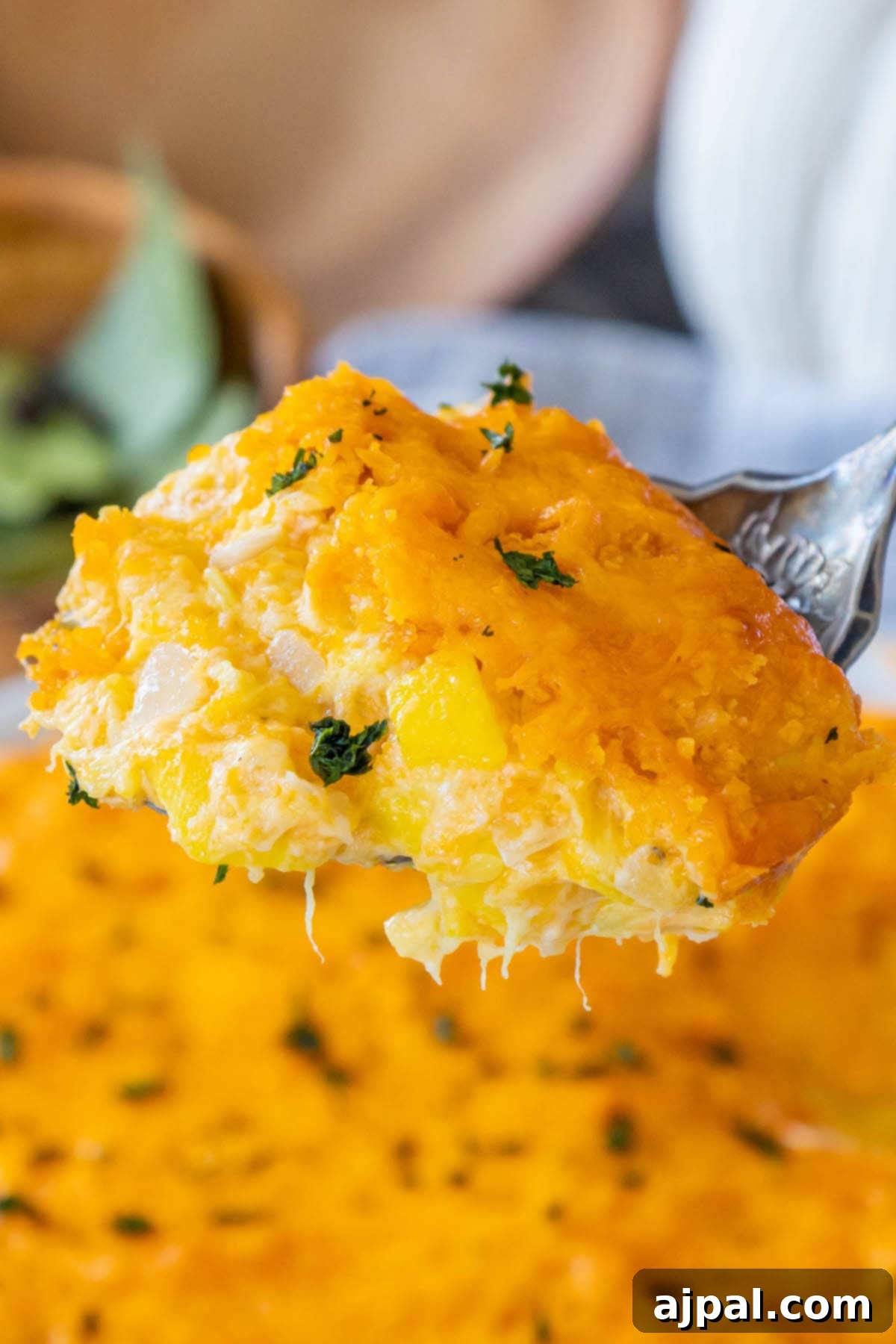 A fork lifts a generous serving of cheesy baked squash casserole from a white dish, showcasing the tender squash, melted cheese, and crispy cracker topping.