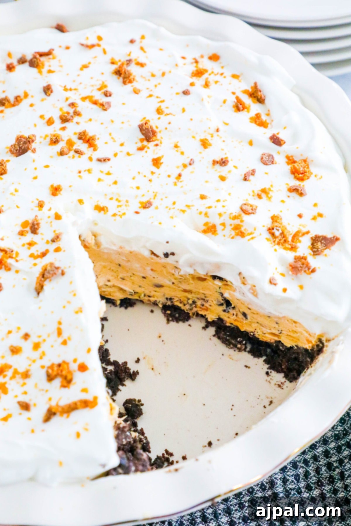 Decadent Butterfinger Pie 2 no bake butterfinger cream pie with an oreo crust in a white pie plate on a table topped with butterfinger candy crumbles