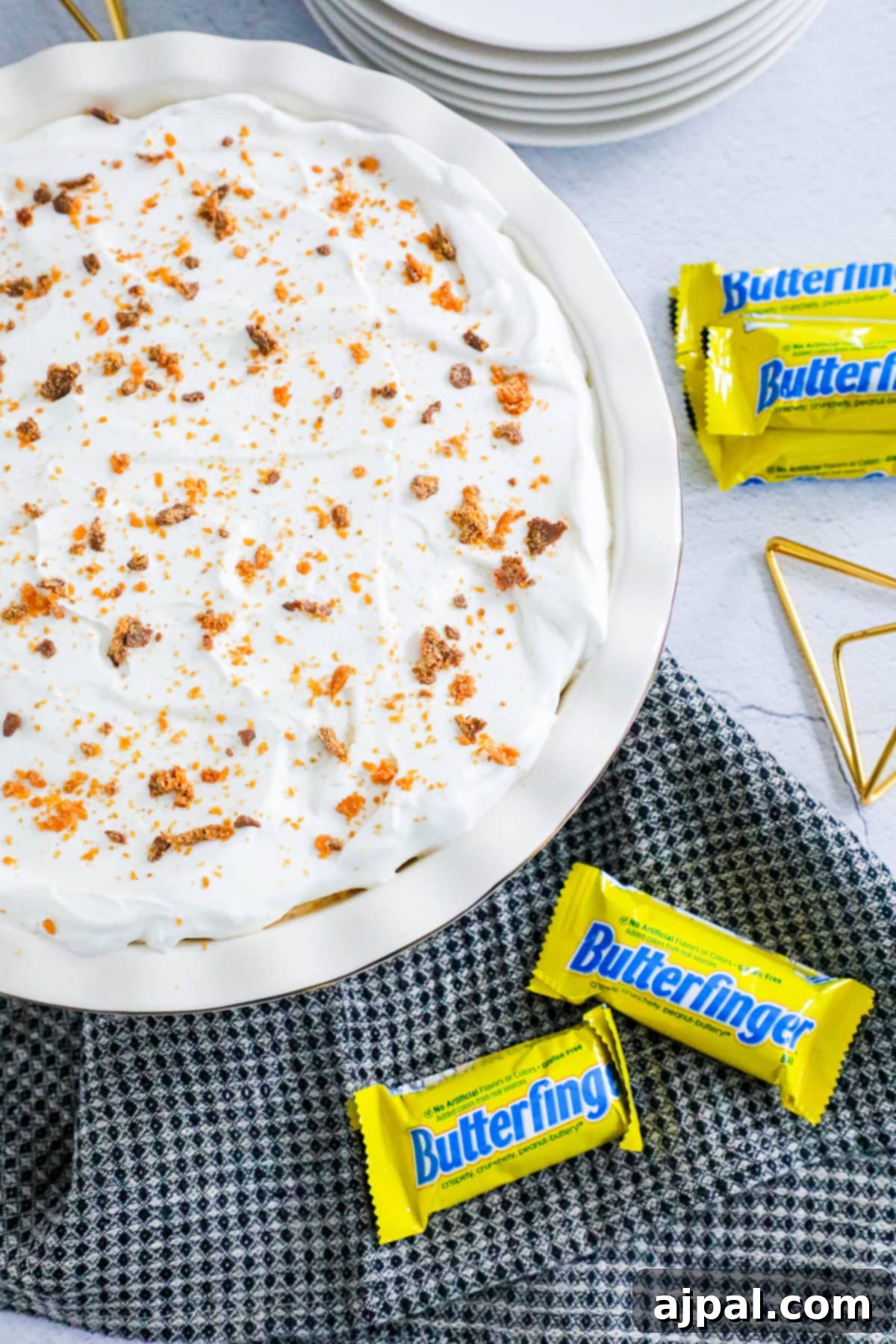 Decadent Butterfinger Pie 3 no bake butterfinger cream pie with an oreo crust in a white pie plate on a table topped with butterfinger candy crumbles
