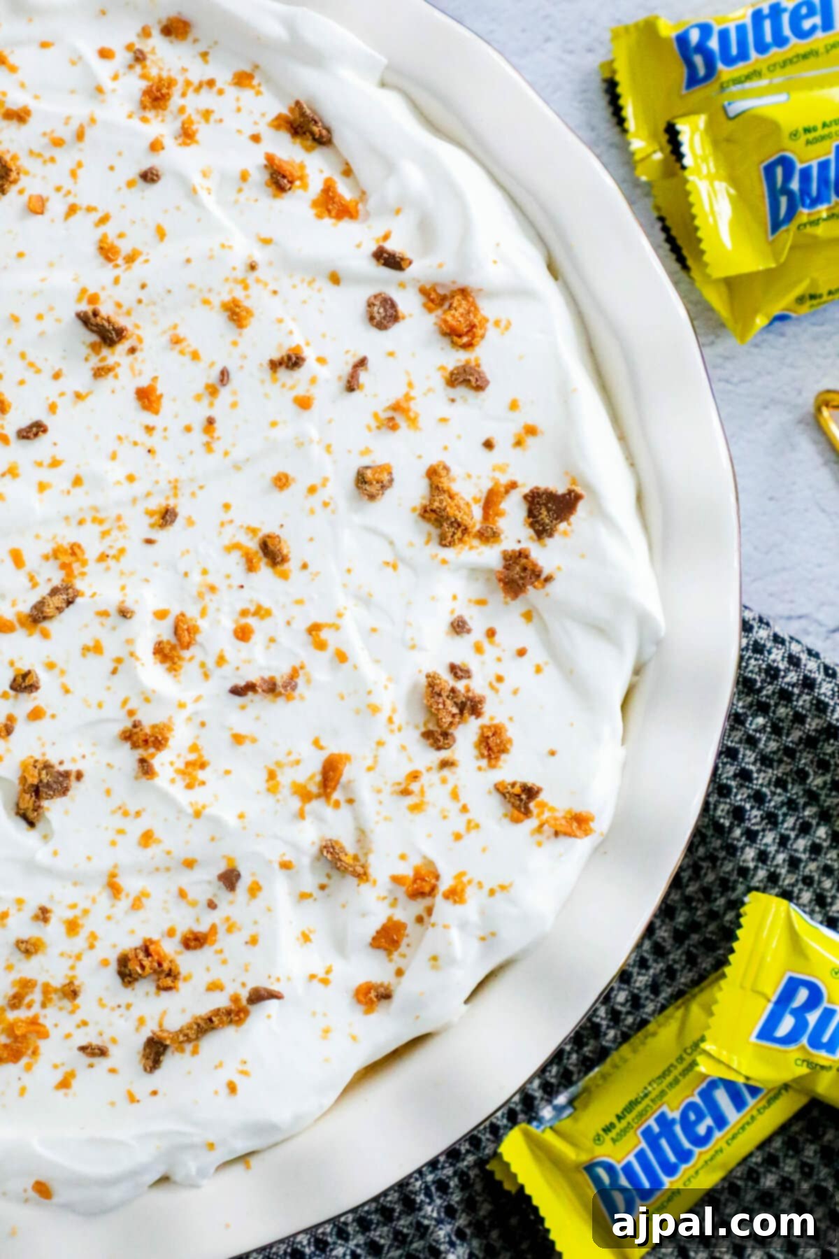 Decadent Butterfinger Pie 7 no bake butterfinger cream pie with an oreo crust in a white pie plate on a table topped with butterfinger candy crumbles