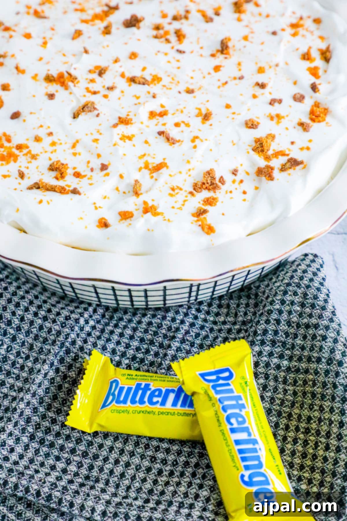Decadent Butterfinger Pie 8 no bake butterfinger cream pie with an oreo crust in a white pie plate on a table topped with butterfinger candy crumbles