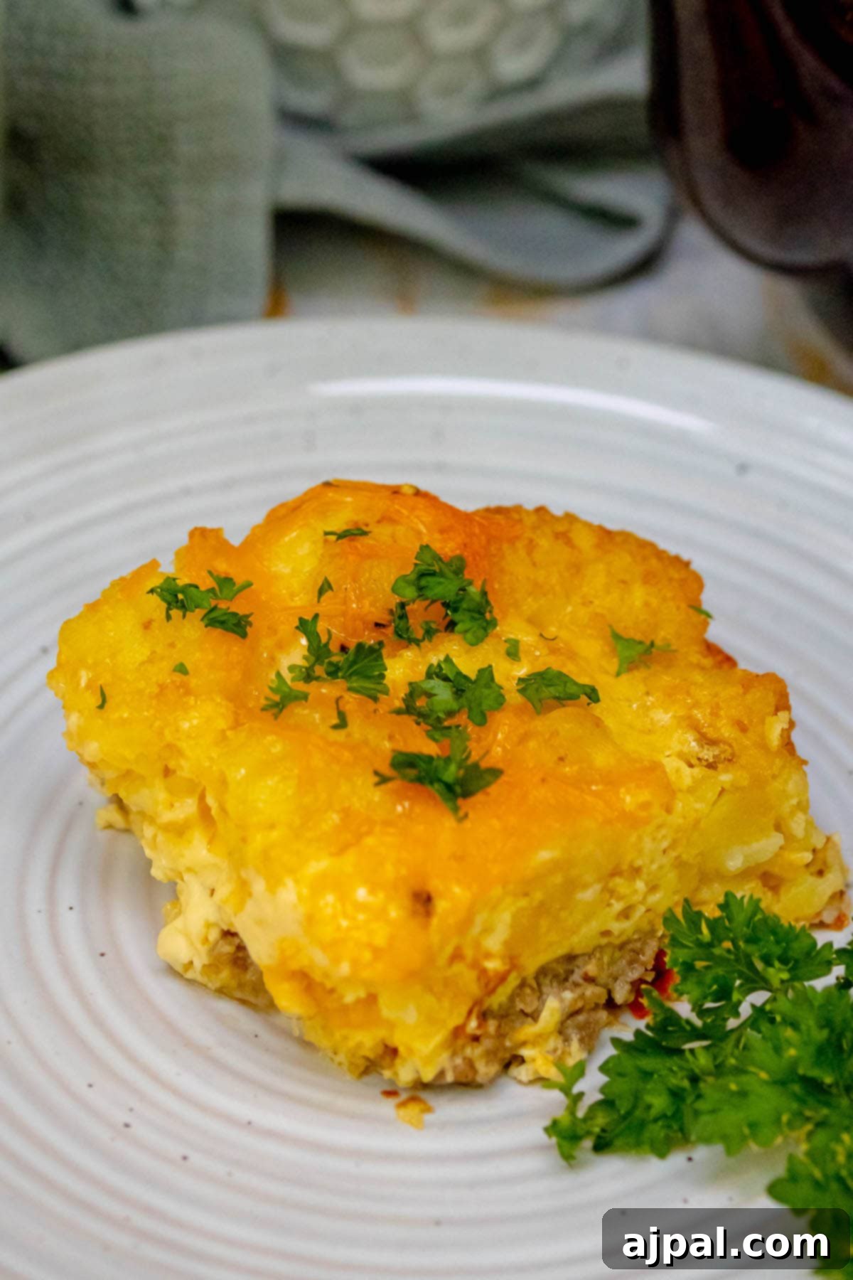 Hearty Tater Tot Breakfast Bake 14 A perfectly baked, cheesy tater tot breakfast casserole, served on a plate with fresh parsley garnish.