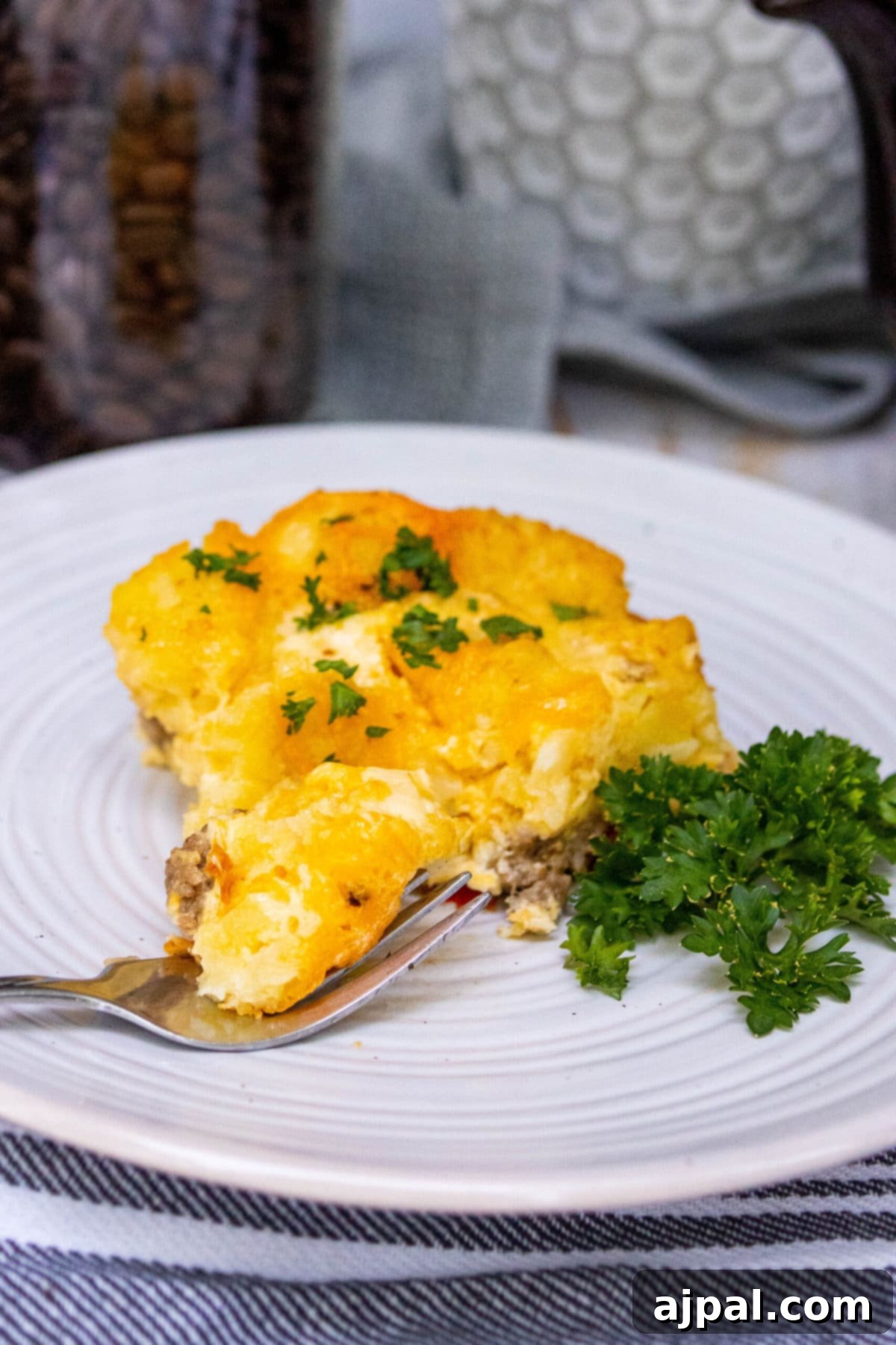 Hearty Tater Tot Breakfast Bake 16 A delicious piece of cheesy baked tater tot casserole on a white plate, ready to be enjoyed.