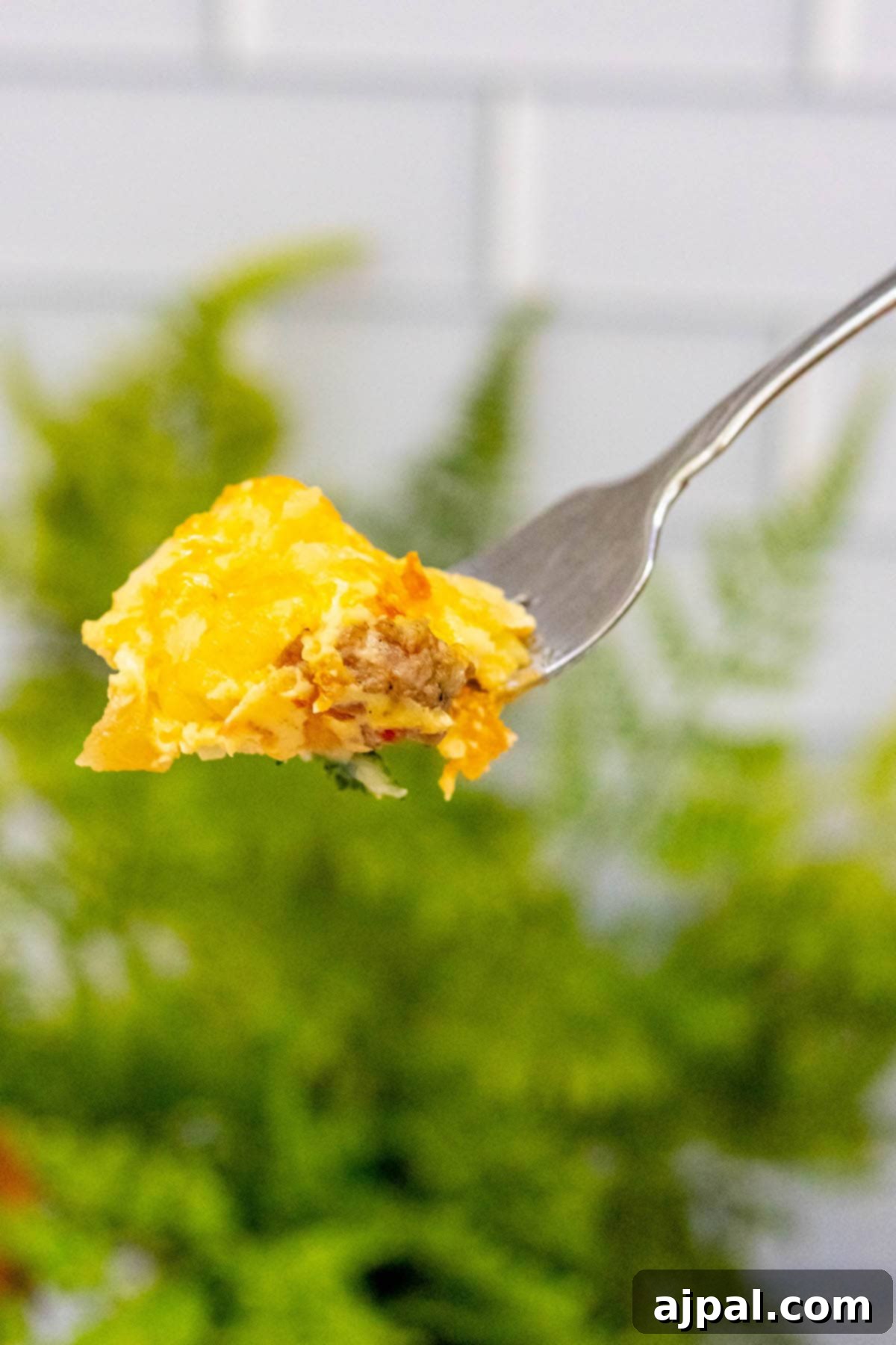 Hearty Tater Tot Breakfast Bake 4 A fork lifts a savory bite of cheesy tater tot casserole, showing the layers of egg, sausage, and potato.