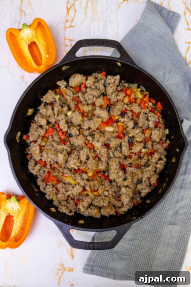 Hearty Tater Tot Breakfast Bake 9 Ground sausage browning with sautéed onions and bell peppers in a skillet, creating a flavorful base.