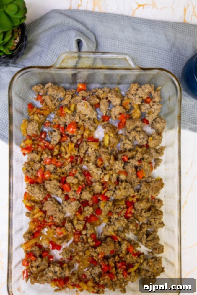 Hearty Tater Tot Breakfast Bake 10 The cooked sausage and vegetable mixture spread evenly at the bottom of a glass baking dish.