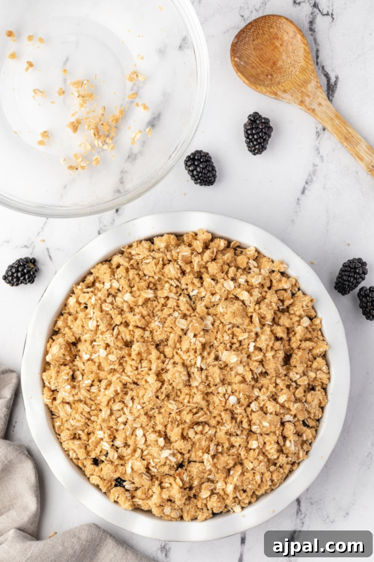 Apple and Blackberry Crumble 8 Blackberry granola in a white bowl next to a wooden spoon with apple crumble ready for baking