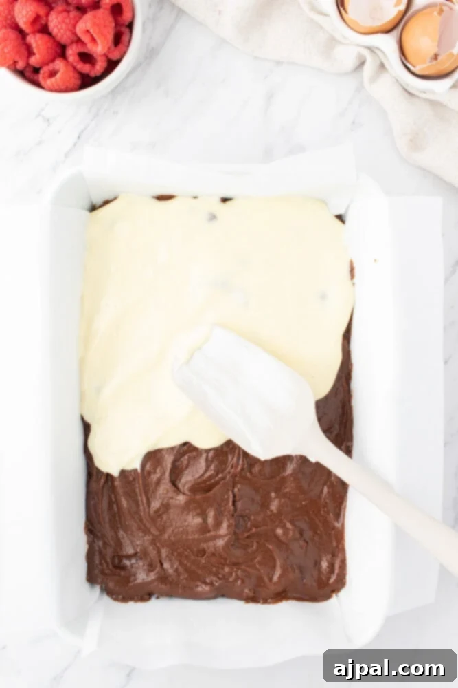 Ultimate Raspberry Cheesecake Brownies 11 spreading cheesecake over brownie batter in a glass dish