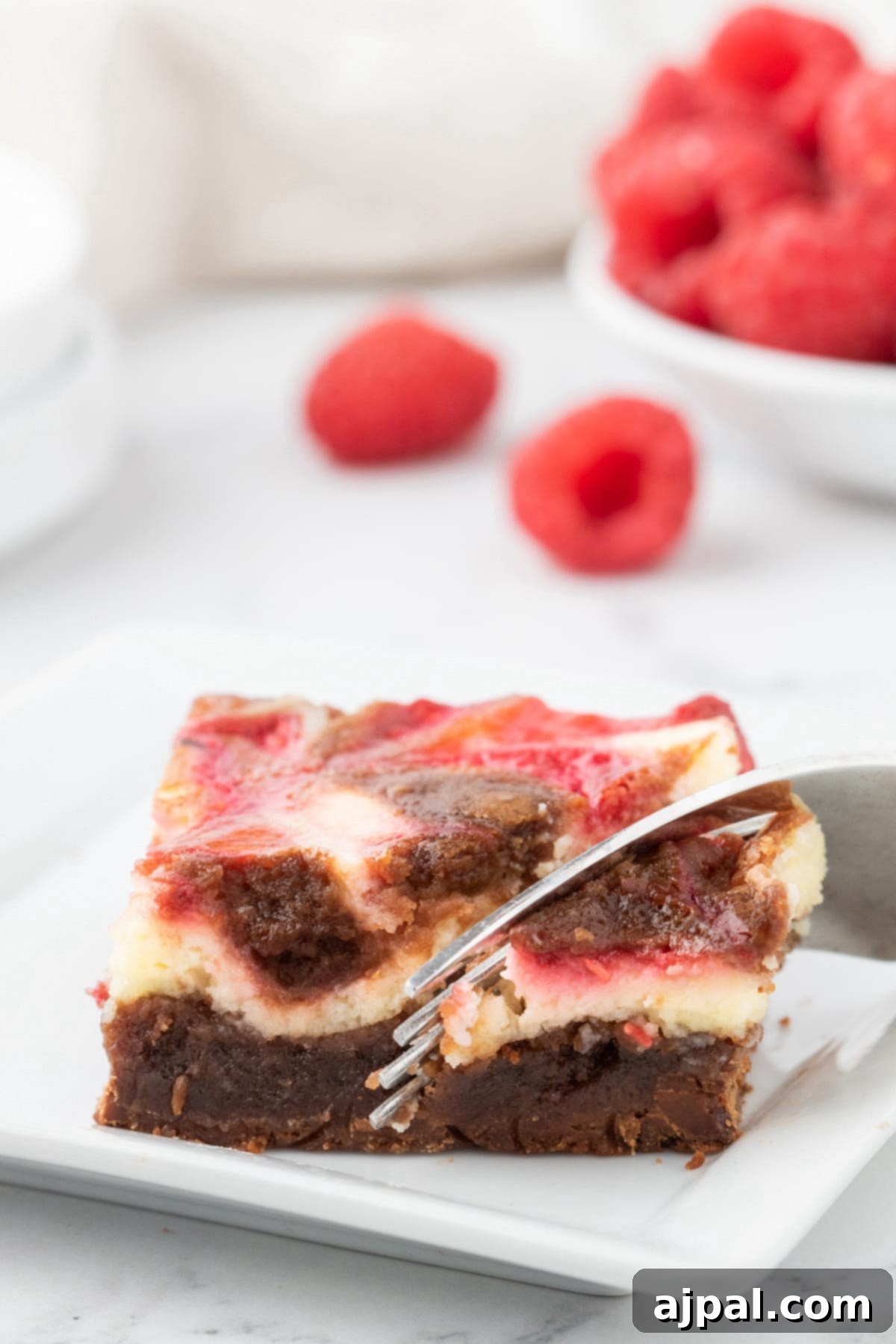 Ultimate Raspberry Cheesecake Brownies 14 A slice of marbled raspberry cheesecake on a white plate.