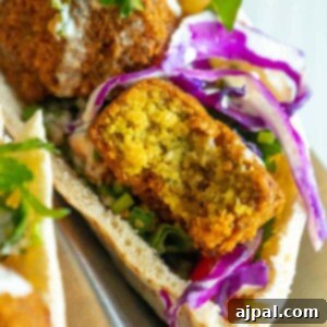 three pitas stuffed with falafel balls, cabbage, and salad with tahini sauce ladled on top