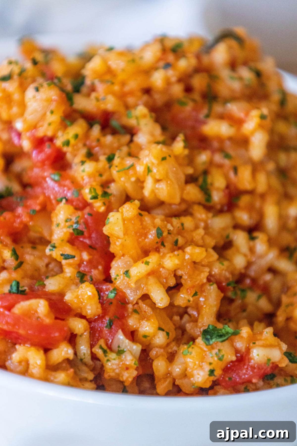 A vibrant bowl of Mexican red rice, garnished with fresh chopped cilantro and diced tomatoes, sits invitingly on a wooden table.