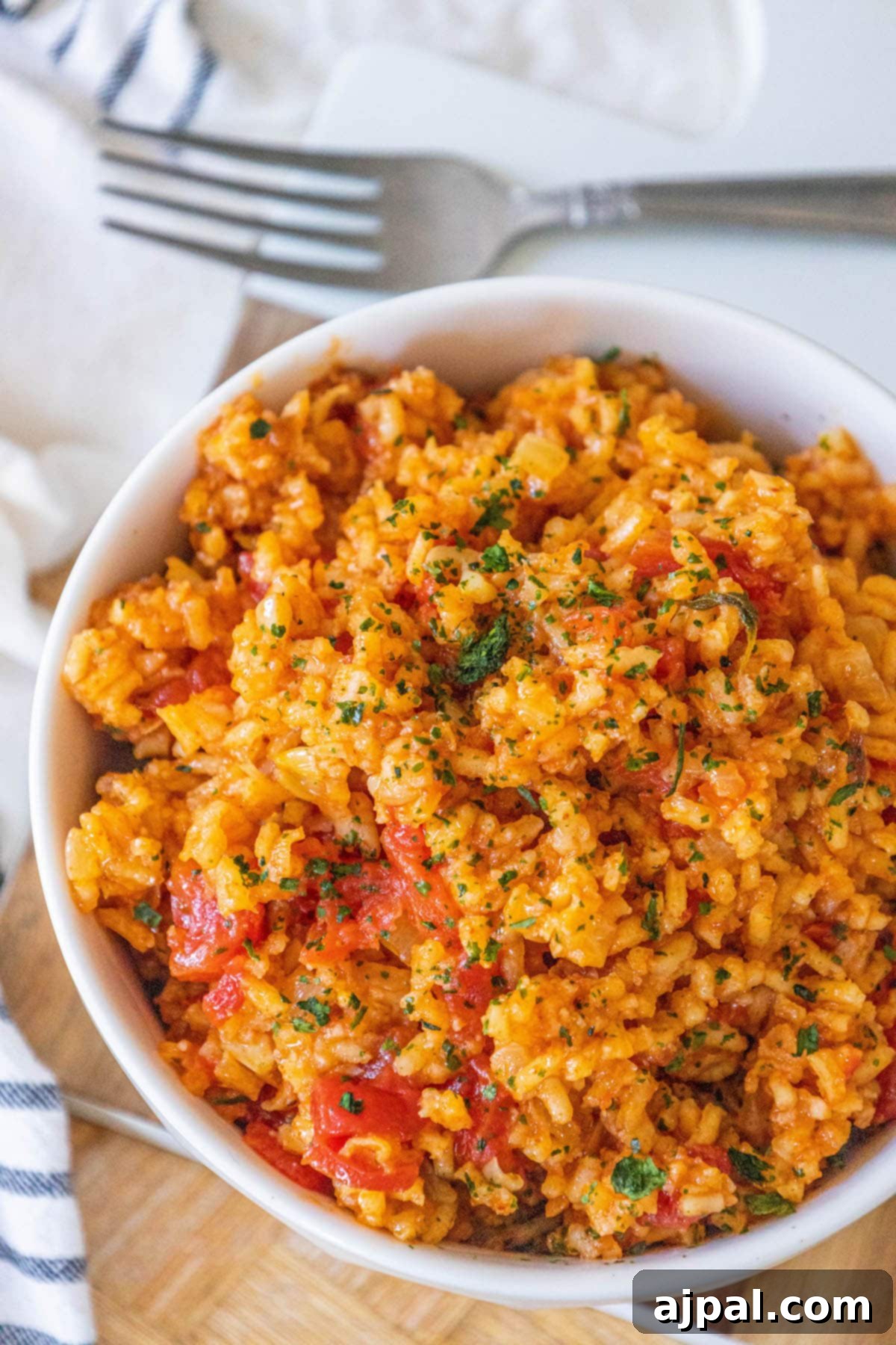 A pristine white bowl overflowing with fluffy red rice, generously studded with vibrant chunks of tomato and fresh green cilantro, set against a simple backdrop.