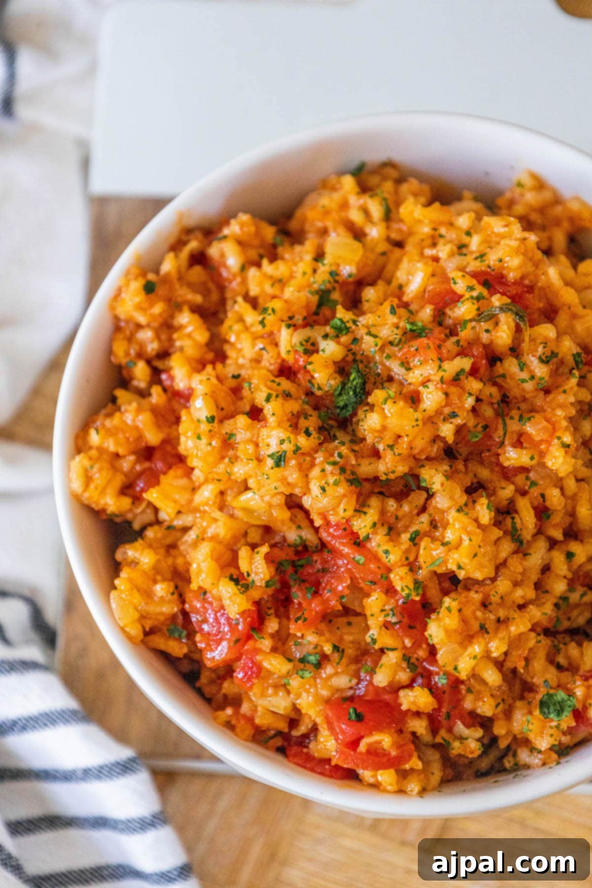 A pristine white bowl filled with vibrant red Mexican rice, garnished with fresh chopped cilantro and diced tomatoes, creating an inviting culinary display.