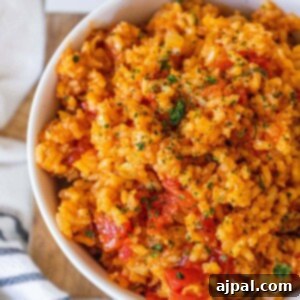 A vibrant bowl of Mexican red rice, garnished with fresh chopped cilantro and diced tomatoes, sits invitingly on a wooden table.