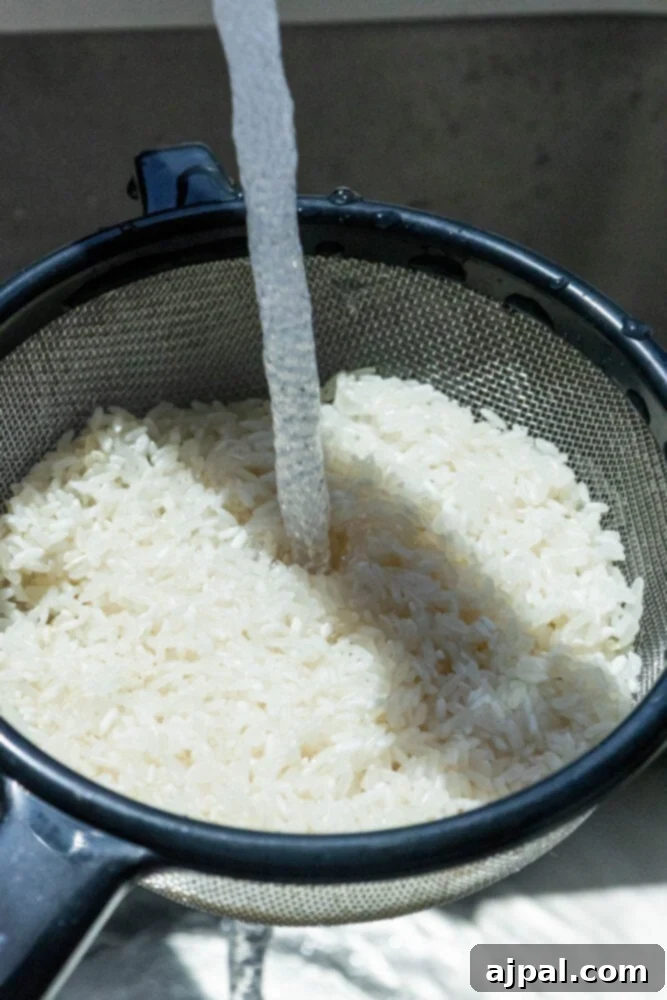A close-up shot of white rice being rinsed under cold water in a metal colander, illustrating the prep step for clean, fluffy grains.